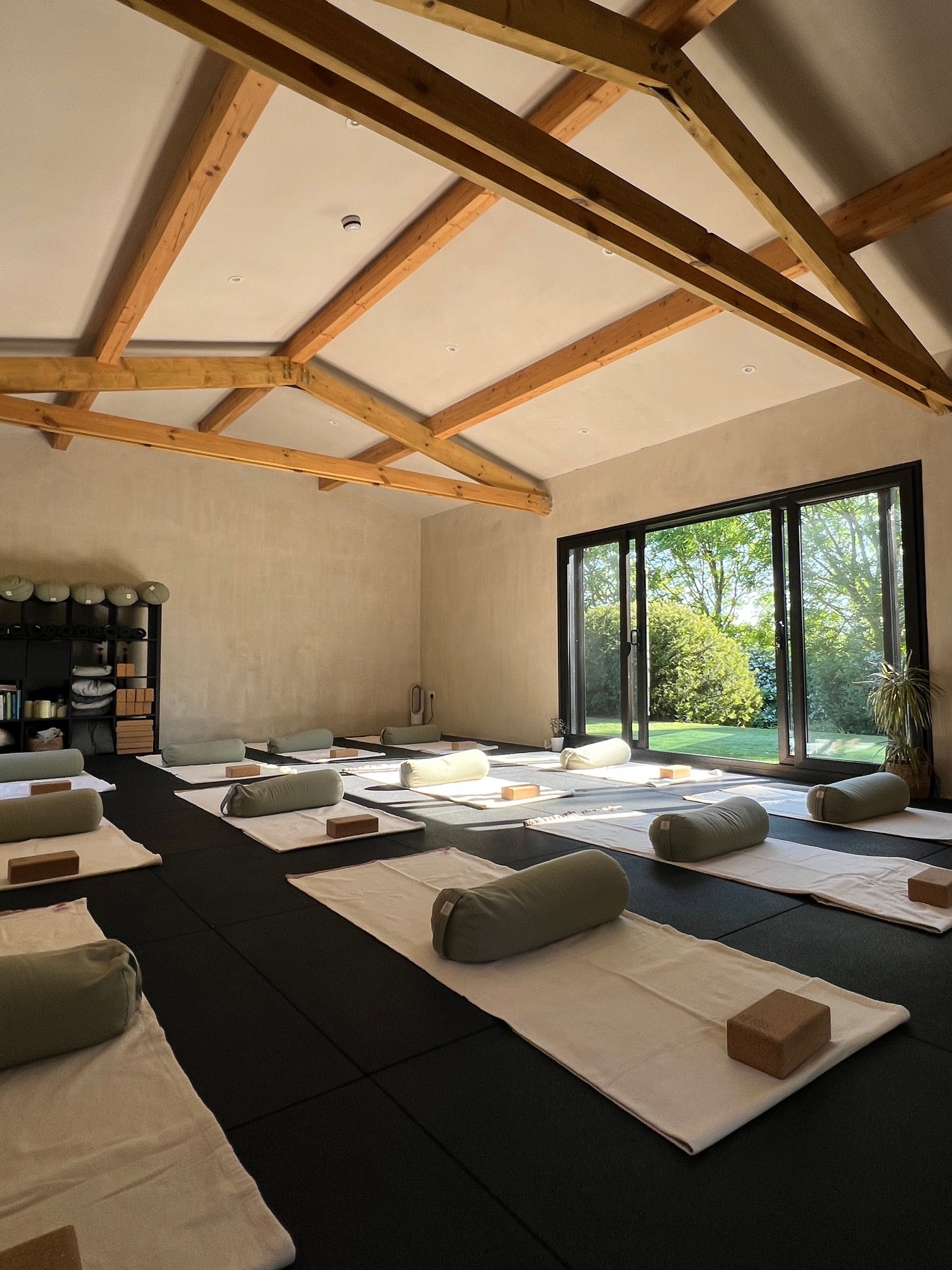 The Devoran studio, empty and ready: mats and bolsters arranged along a charcoal floor beneath exposed timber beams.